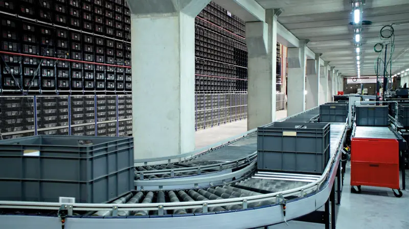 Grey totes on a curved conveyor in front of a miniload storage system